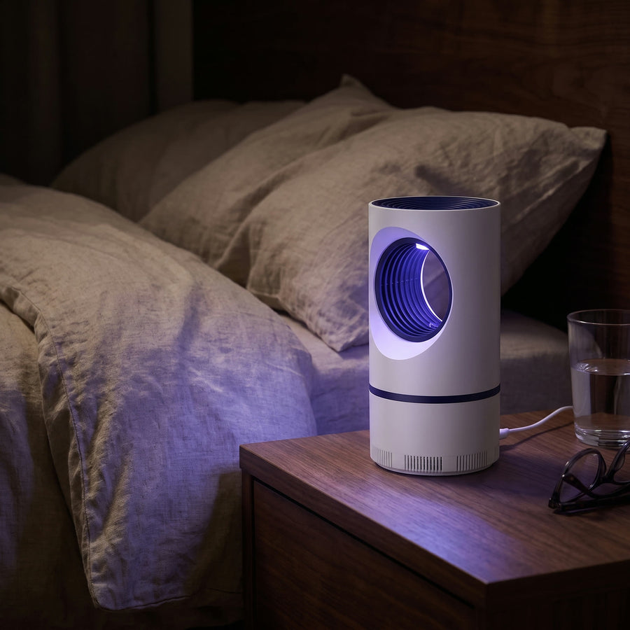 Nightfall mosquito trap glowing violet on a bedside table at night beside linen bedding